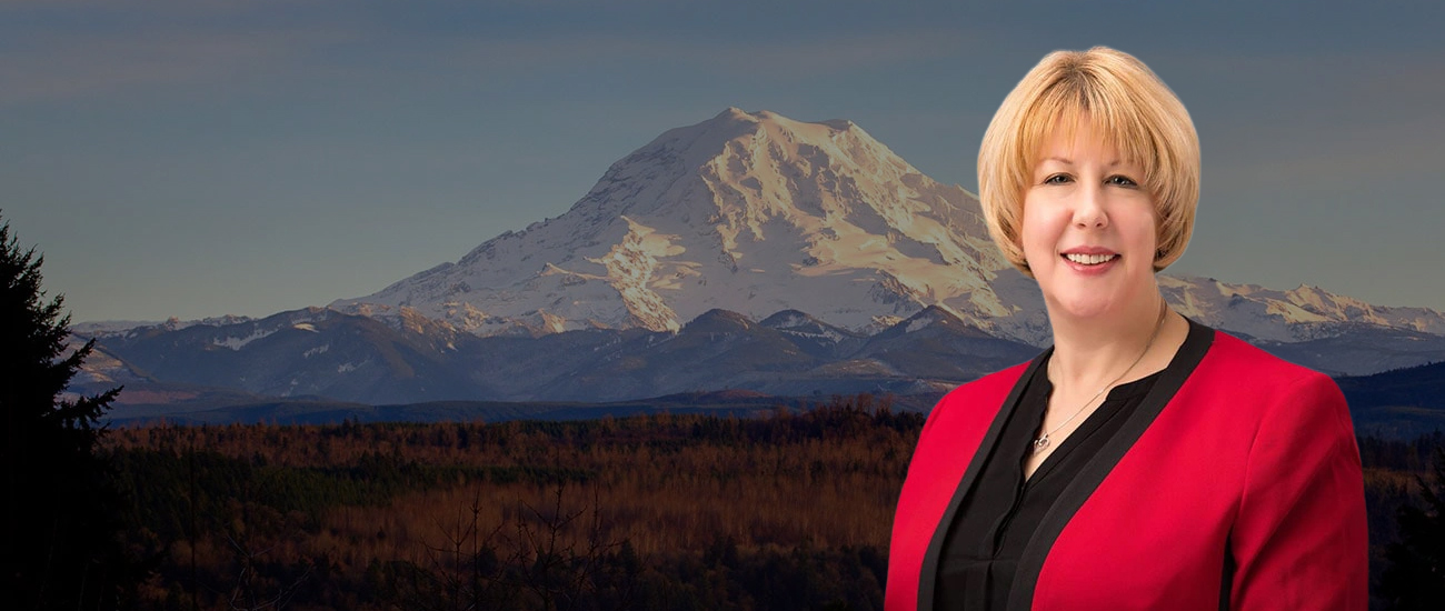 Attorney Laurie G. Robertson in a red blazer with a scenic view of Mount Rainier in the background